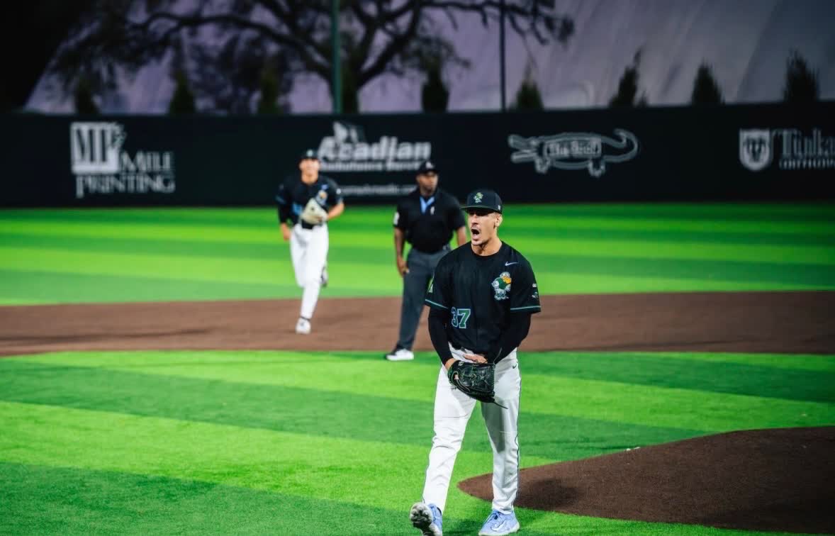 Jake Toporek on the mound in his Missoula PaddleHeads uniform, shouting after a play, with a teammate and the umpire behind him